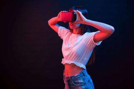 Young woman using virtual reality glasses in the dark room with neon lighting.