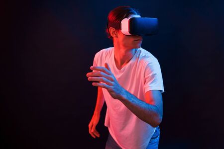 Active leisure. Young man using virtual reality glasses in the dark room with neon lighting.の写真素材