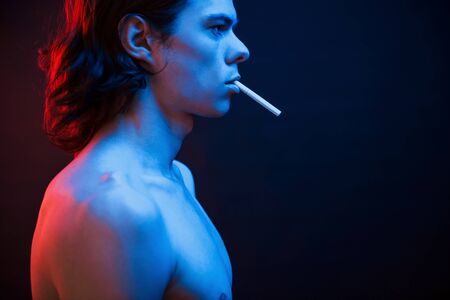 Good looking guy. Studio shot in dark studio with neon light. Portrait of serious man.の写真素材