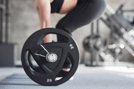 Taking weight. Cropped photo of woman doing squatting with barbell in the gym.の写真素材