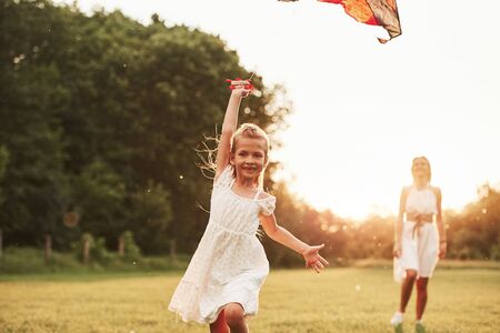 Front view. Mother and daughter have fun with kite in the field. Beautiful nature.の写真素材