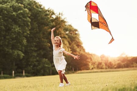 Going forward. Happy girl in white clothes have fun with kite in the field. Beautiful nature.の写真素材