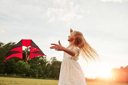 Almost clear sky. Happy girl in white clothes have fun with kite in the field. Beautiful nature.の写真素材