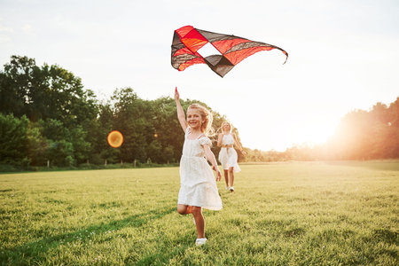 Kid is smiling. Mother and daughter have fun with kite in the field. Beautiful nature.の写真素材