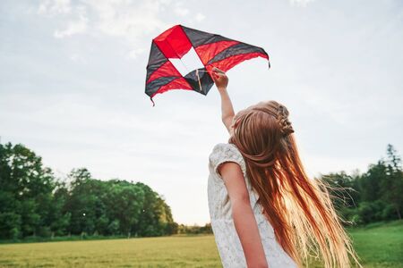 Let it fly. Happy girl in white clothes have fun with kite in the field. Beautiful nature.の写真素材