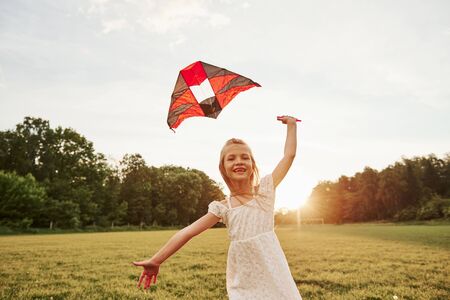 Running to the camera. Happy girl in white clothes have fun with kite in the field. Beautiful nature.の写真素材