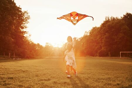 Right in the sky. Mother and daughter have fun with kite in the field. Beautiful nature.の写真素材