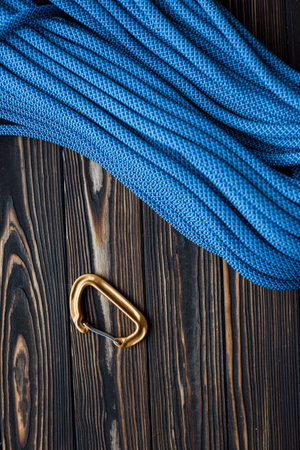 Under long blue knot. Isolated photo of climbing equipment. Part of carabiner lying on the wooden...