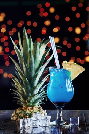 Top of pinaple lying near drink. Cocktail is ready. On the wooden table in the night club. Nice lighting.の写真素材