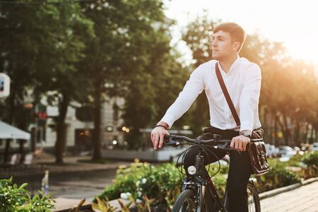 Summer green trees at background. Businessman in formal clothes with black bicycle is in the city.の写真素材