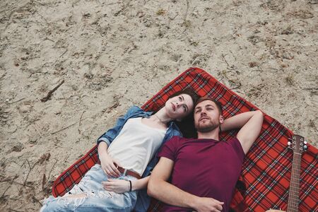 Looking up. Young couple have picnic on the beach. Lying on the red colored blanket.の写真素材