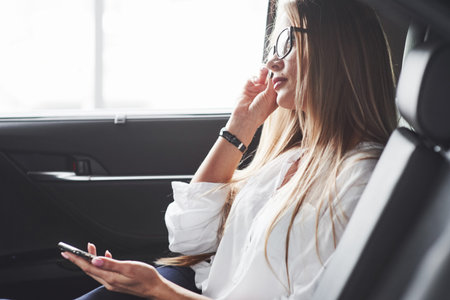 Touches glasses. Beautiful blonde girl sitting in the new car with modern black interior.