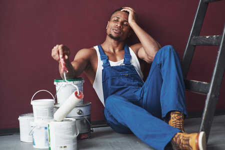 Waiting for helper. Young african american worker in blue uniform have a break on his job.