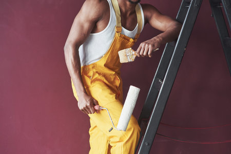 Tools in hands. Young african american worker in the yellow uniform have some job.