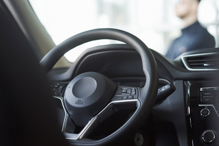 Inside of brand new black car. Luxury interior. Man stands in front of automobile.