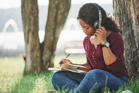 With new wireless headphones. Cheerful african american woman in the park at summertime.の写真素材