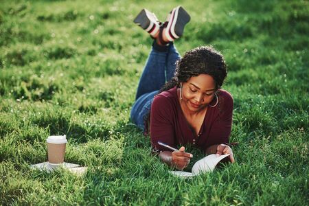 Taking notes. Cheerful african american woman in the park at summertime.の写真素材