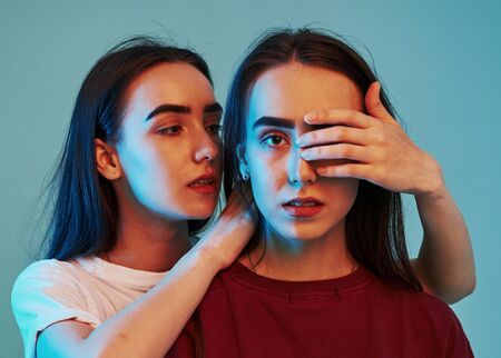 Lets keep it a secret. Studio shot indoors with neon light. Photo of two beautiful twins.の写真素材