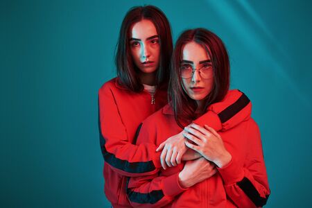 In red wear. Studio shot indoors with neon light. Photo of two beautiful twins.の写真素材