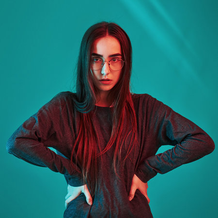 Hands on waist. Studio shot indoors with neon light. Portrait of beautiful young girl.