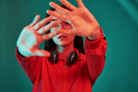 Keeps hands in front of camera. Studio shot indoors with neon light. Portrait of beautiful young girl.の写真素材