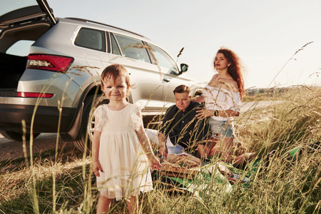 Enjoying nature. Family have picnic at countryside near silver automobile at sunset.の写真素材