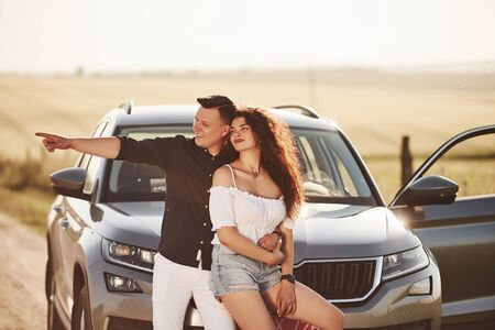 Shows something by the hand. Lovely couple near their new modern car at weekend time.の写真素材