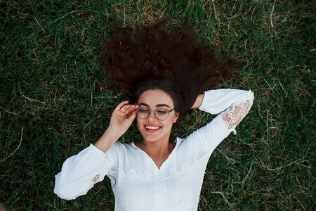Looks through new sunglasses. Girl lying down on the green grass and have a rest.の写真素材