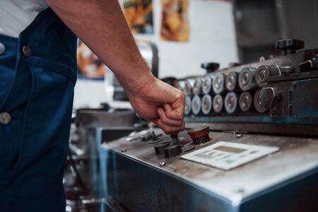 Turns on the machine. Man in uniform works on the production. Industrial modern technology.の写真素材