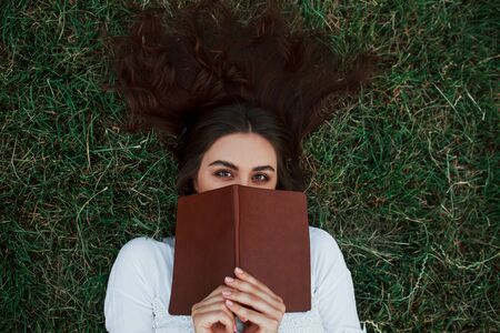 Hiding behind the book. Girl lying down on the green grass and have a rest.の写真素材