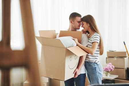 Box with smile painted on it. Cheerful young couple in their new apartment. Conception of moving.