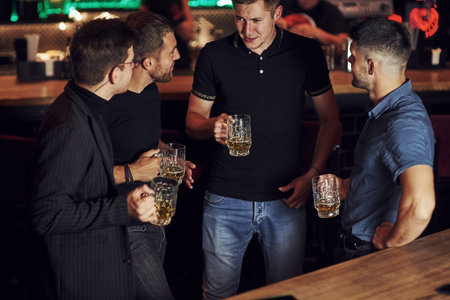 Warm atmosphere. Friends resting in the pub with beer in hands. Having conversation.の写真素材