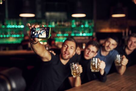 Making a selfie. Three friends resting in the pub with beer in hands. Having conversation.の写真素材