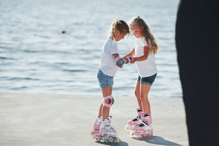 Two kids learning how to ride on roller skates at daytime near the lake.