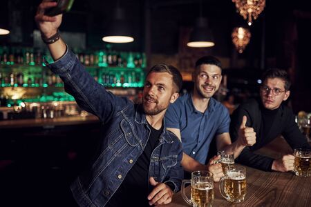 Making selfie. Three sports fans in a bar watching soccer. With beer in hands.の写真素材