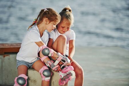 Two little girls with roller skates outdoors near the lake at background.の写真素材