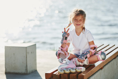 Cute little girl with roller skates outdoors near the lake at background.