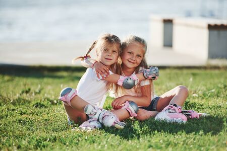 Kids embracing when sitting on the grass in the park. In roller skates.の写真素材