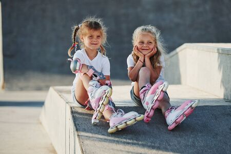 Having a rest. On the ramp for extreme sports. Two little girls with roller skates outdoors have fun.の写真素材