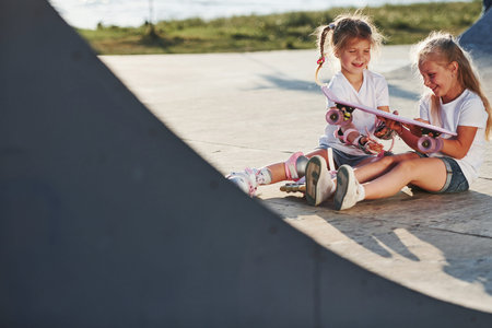 Relaxing and have conversation. On the ramp for extreme sports. Two little girls with roller skates outdoors have fun.の写真素材