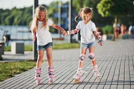 Two cute kids riding by roller skates in the park at daytime.の写真素材