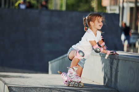 Cute little girl with roller skates outdoors sits on the ramp for extreme sports.の写真素材