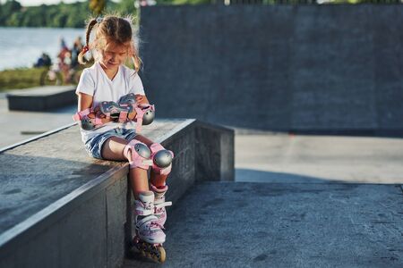 Cute little girl with roller skates outdoors sits on the ramp for extreme sports.の写真素材