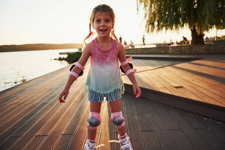 Happy cute kid riding on her roller skates. Summertime leisure and weekends.