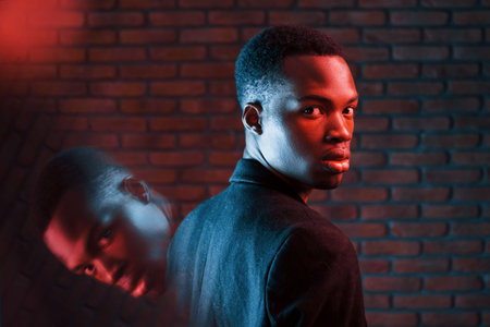 Beautiful reflection. Futuristic neon lighting. Young african american man in the studio.