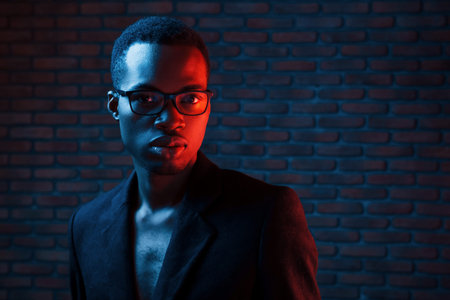 In eyewear. Futuristic neon lighting. Young african american man in the studio.の写真素材