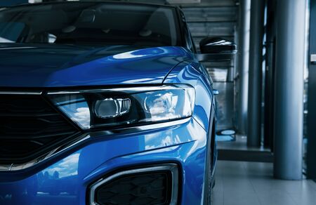 Front part of brand new modern blue car. Parked at showroom. Reflection in the headlights.の写真素材