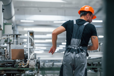 Taking the window. Industrial worker indoors in factory. Young technician with orange hard hat.