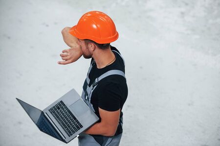 Aerial view. With laptop in hands. Industrial worker indoors in factory. Young technician with orange hard hat.の写真素材