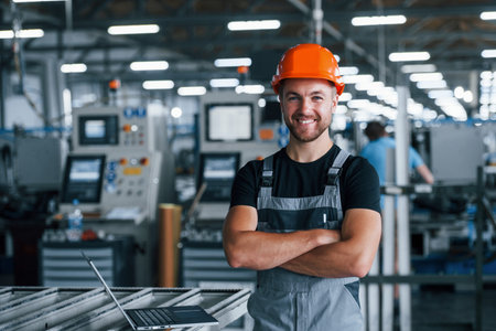 Smiling and happy employee. Industrial worker indoors in factory. Young technician with orange hard hat.の写真素材